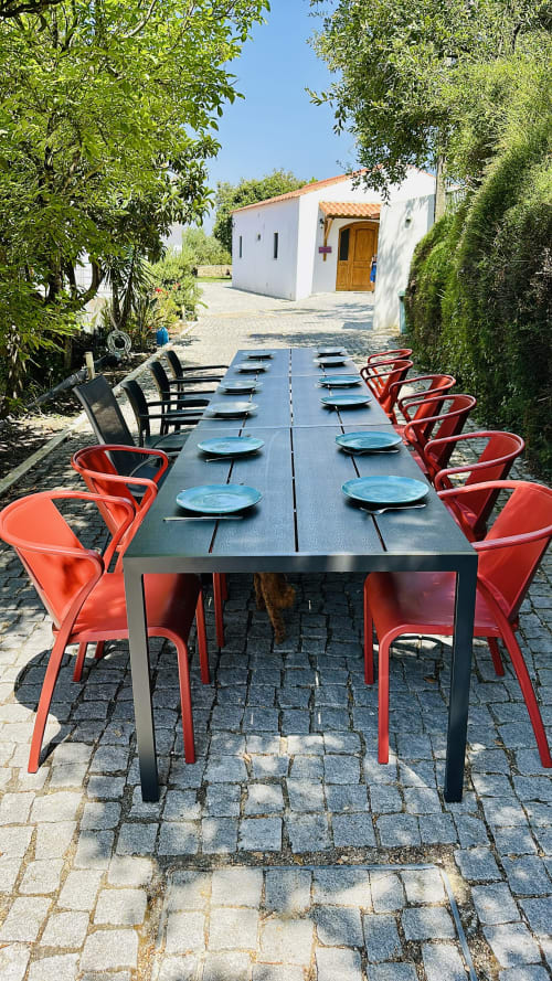 Outdoor dining setup at Quinta Boa Vida cottage in Alcobaça with long table, red chairs, and blue place settings