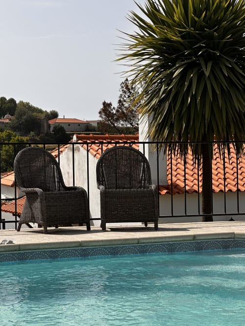 Two wicker chairs by turquoise pool at Quinta Boa Vida cottage, Alcobaça Portugal with terracotta roofs
