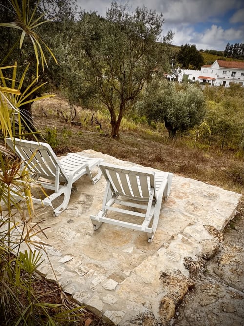 White lounge chairs on stone terrace overlooking olive grove gardens at Quinta Boa Vida, Alcobaça