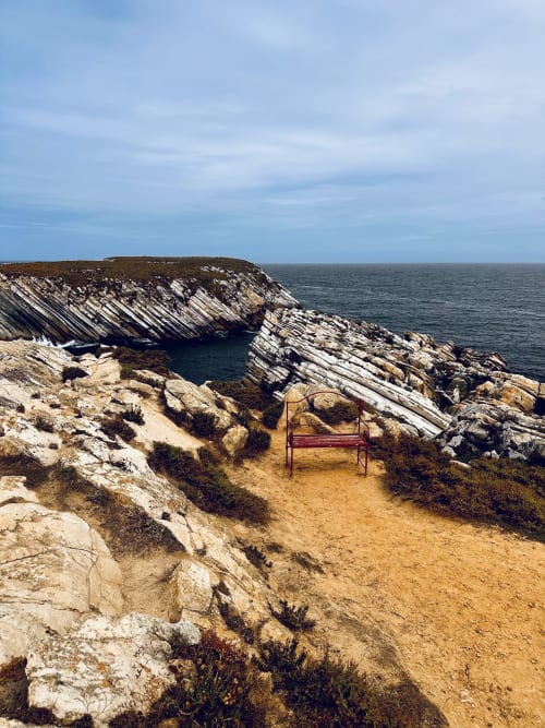 Red bench overlooking dramatic coastal cliffs and turquoise waters at Quinta Boa Vida, Alcobaça Portugal
