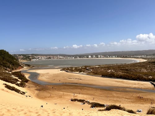 Panoramic coastal view of Alcobaça beach with sandy shores, tidal channels, and town buildings along the coastline under blue