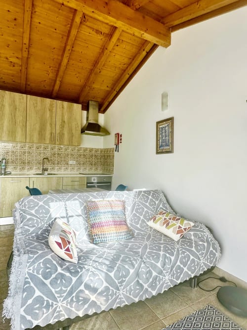 Cozy studio with wooden beams, kitchenette, and sofa with patterned throw at Quinta Boa Vida, Alcobaça