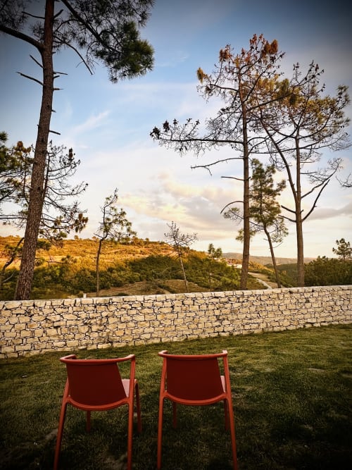Two red chairs on grass overlooking stone wall and forested hills at Quinta Boa Vida, Alcobaça Portugal