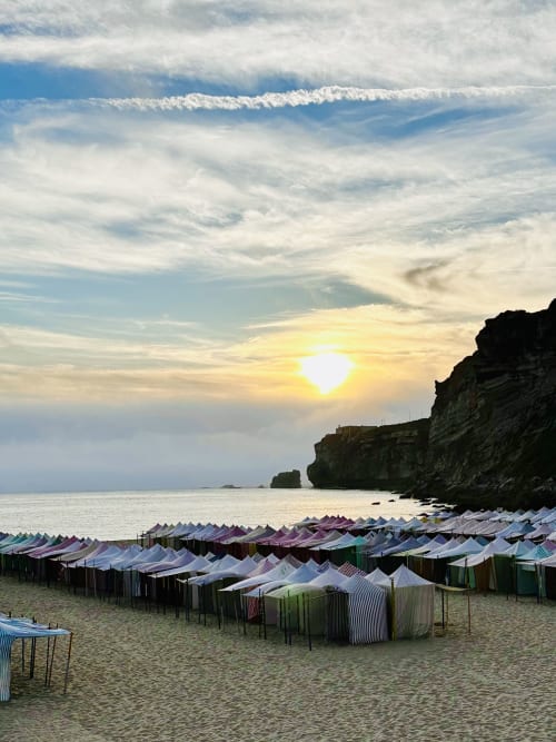 Sunset over beach with colorful striped tents and rocky cliffs, Alcobaça Portugal
