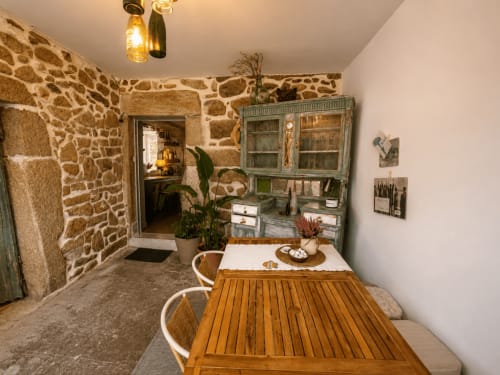 Comedor de la casa Mirada do Roxo en Holibai, Baiona con muros de piedra, mesa de madera y acceso a terraza con vistas al mar