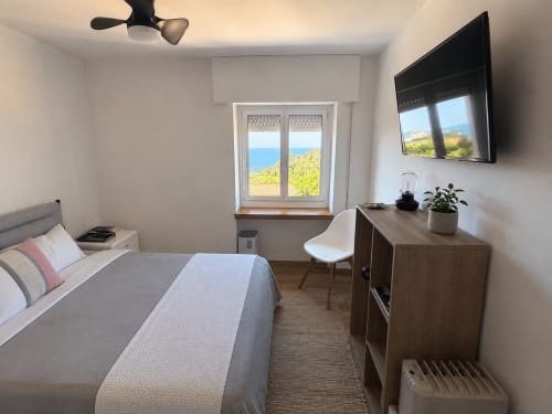 Dormitorio moderno con vistas al mar en cabaña de Baiona, con cama, escritorio, TV y ventana costera panorámica