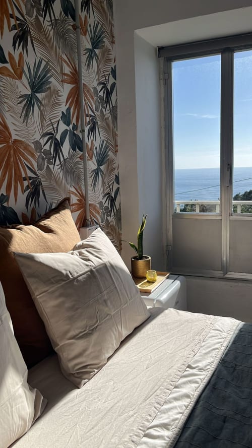 Luminoso dormitorio en casa rural Holibai en Baiona con vistas al mar, papel pintado tropical, ropa de cama blanca y balcón con vistas