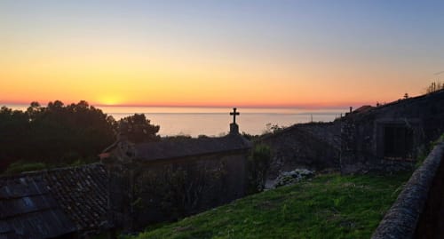 Atardecer sobre el mar de Baiona visto desde la casita Mirada do Roxo con cruz y ruinas de piedra