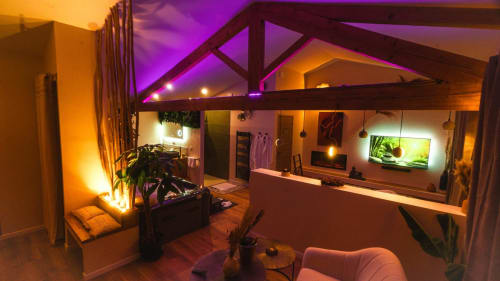 Suite moderne aux lumières ambiantes mauve et orange, sauna, TV, plantes et sièges confortables à Suite l'Olive Sacrée