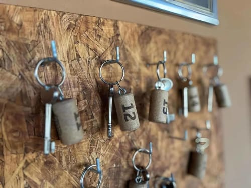 Porta-chaves de cortiça com etiquetas numeradas penduradas em painel de madeira texturizada na adega Tranca da Barriga em Covilhã