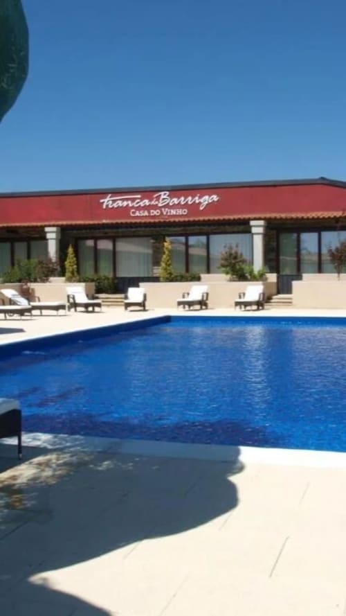 Piscina da Tranca da Barriga Casa do Vinho, pousada vinícola em Covilhã, Portugal, com espreguiçadeiras e edifício de telhado vermelho