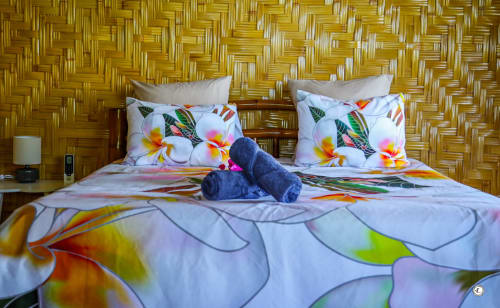 Chambre tropicale colorée avec parure de lit florale éclatante, oreillers moelleux et mur tressé jaune à Aimehome Teavaro