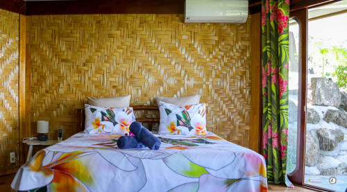 Chambre de villa tropicale Aimehome Location avec literie florale, mur en bois tressé et accès vue mer à Teavaro
