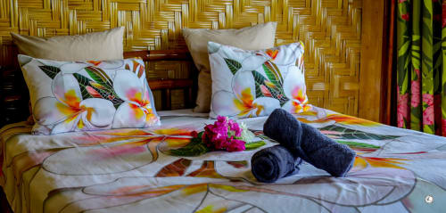Chambre Villa Kia Ora avec literie florale tropicale, serviettes moelleuses, fleurs fraîches, tête de lit tissée, vue sur mer chez Aimehome