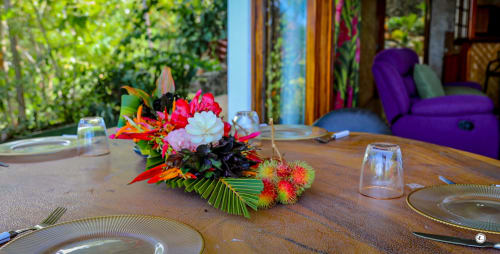 Composition florale tropicale ornant la table à diner de la Villa Kia Ora House à Teavaro, avec vue sur le jardin