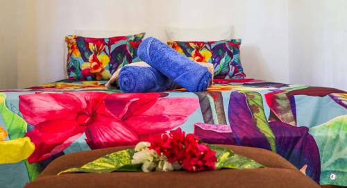 Literie tropicale colorée aux motifs floraux et serviettes bleues roulées à la villa Aimehome, Teavaro
