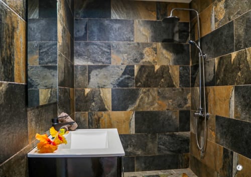 Salle de bains luxueuse avec murs en ardoise, baignoire îlot blanche, douche pluie et fleurs jaunes à la villa Aimehome à Teavaro