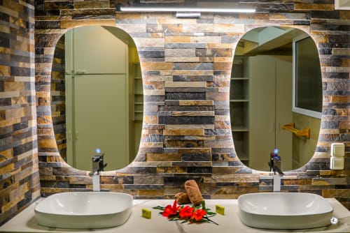 Salle de bains double vasque à la Villa Kia Ora, Aimehome Teavaro : miroirs ovales, carrelage en pierre et vasques blanches.
