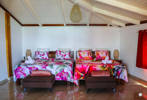 Chambre lumineuse de villa avec deux lits aux draps floraux rose vif, poutres en bois et suspension tissée chez Aimehome