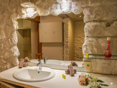 Salle de bains luxueuse avec double vasque, murs en pierre et fleurs tropicales à la villa Aimehome à Teavaro