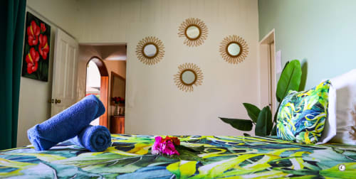 Chambre lumineuse de villa Aimehome avec literie tropicale colorée, serviettes bleues, miroirs décoratifs en forme de soleil et fleurs vibrantes