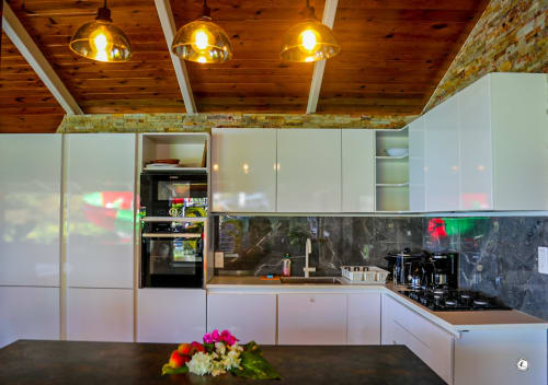 Cuisine moderne de la villa Aimehome à Teavaro : mobilier blanc, crédence noire, plafond en bois et suspensions