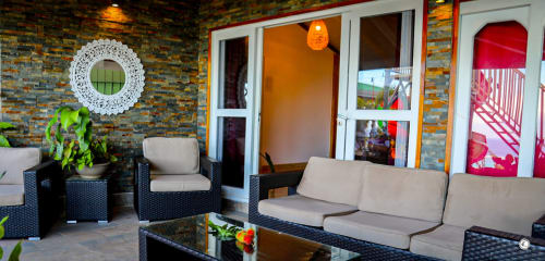 Salon moderne de la villa Aimehome Teavaro avec meubles tressés, plantes tropicales et portes offrant une vue sur la mer