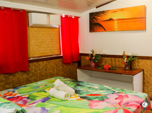 Chambre tropicale colorée à la villa Aimehome à Moorea avec literie éclatante, rideaux rouges et art mural coucher de soleil