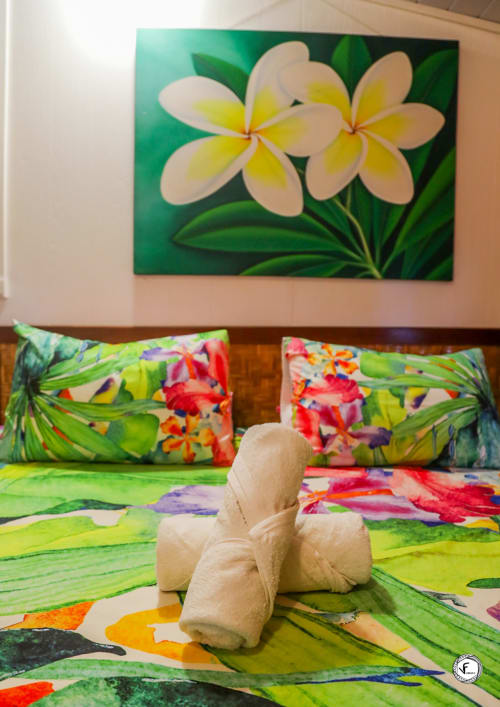 Chambre de villa tropicale à Moorea avec fleurs de frangipanier blanc peintes sur toile, literie florale colorée et rouleaux