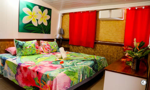 Chambre tropicale colorée à Aimehome à Moorea avec parure florale vibrante, vue sur mer et rideaux rouge vif