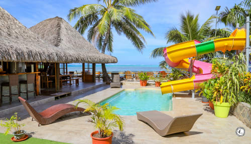 Villa tropicale à Moorea avec piscine turquoise, bungalow à toiture de chaume, toboggan coloré et vue sur l'océan