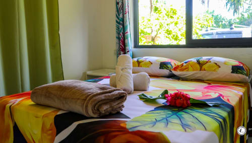 Chambre de villa tropicale colorée à Moorea avec literie vibrante, serviette roulée et fleurs rouges surplombant la vue sur mer