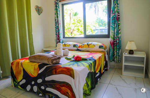 Chambre tropicale colorée à la villa Aimehome à Moorea avec literie éclatante, rideaux verts et vue océan