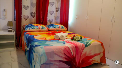 Literie florale colorée à la villa de Moorea avec rideaux rouges, serviettes jumelées et armoire blanche.