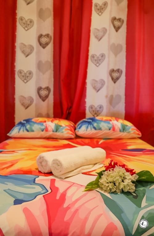 Literie tropicale colorée avec serviettes roulées et fleur blanche sur le lit de la villa Aimehome à Moorea