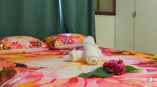 Literie florale colorée à la villa Fare Kuuheiura d'Aimehome à Moorea avec serviettes roulées et fleur rose sur le lit