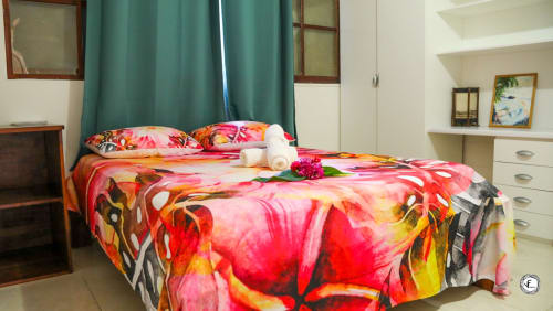 Chambre de la villa Fare Kuuheiura à Aimehome, Moorea : linge de lit floral coloré, rideaux bleu-vert et étagères de rangement blanches