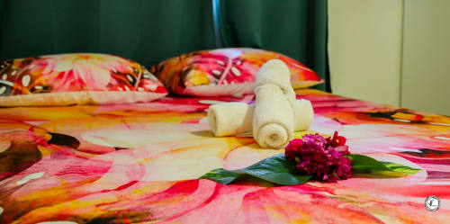 Literie tropicale colorée avec serviettes blanches roulées et fleur magenta sur le lit de la villa de Moorea