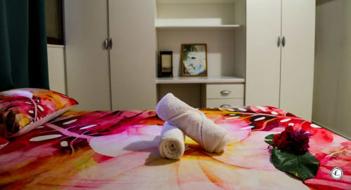 Linge de lit tropical coloré avec serviettes roulées et fleur rouge sur lit de villa à Moorea, armoire blanche