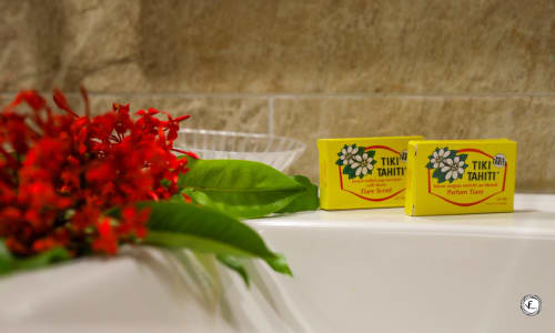 Produits de toilette Tiki Tahiti et fleurs rouges sur le comptoir de la salle de bain de la villa Aimehome à Moorea