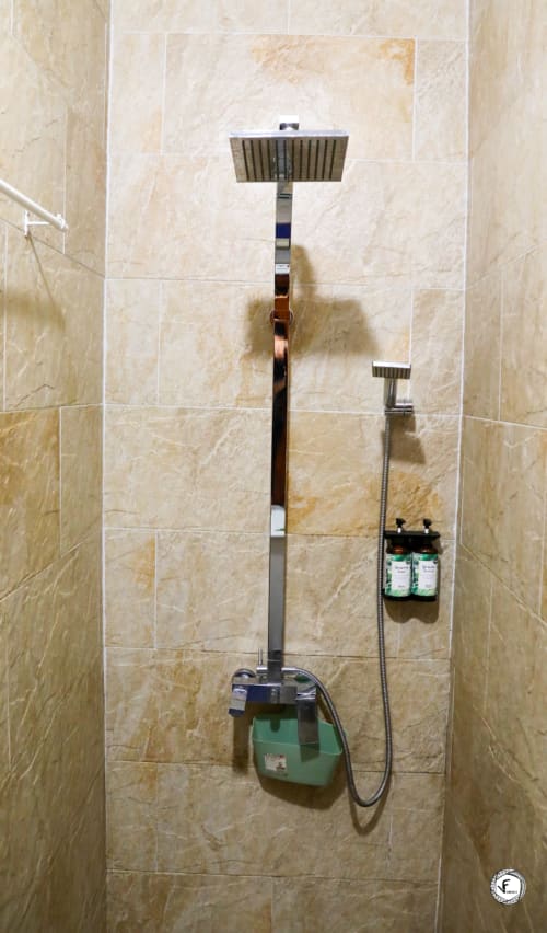 Salle de bain moderne à Moorea avec douche pluie, pommeau manuel et accessoires de toilette sur carrelage beige