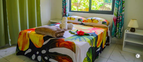 Chambre de villa colorée à Moorea avec parure florale éclatante, rideaux tropicaux, accents verts et vue sur mer