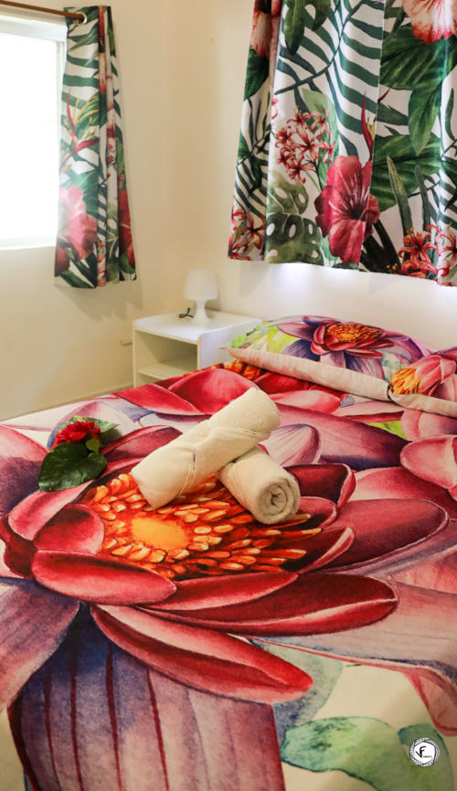 Chambre de villa tropicale à Aimehome Moorea avec literie florale éclatante, serviettes roulées et rideaux botaniques