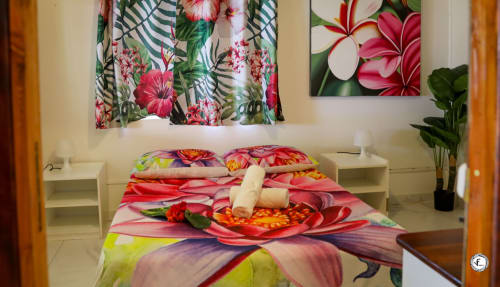Literie florale colorée dans villa de Moorea avec décor tropical, tables de nuit blanches et art mural artistique
