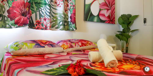 Chambre tropicale colorée à Aimehome, Moorea avec literie florale, coussins décoratifs et plantes luxuriantes