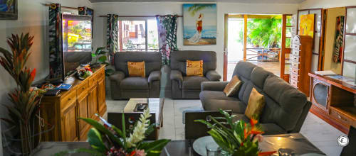 Spacieux séjour de villa à Moorea avec sièges gris, mobilier en bois, plantes tropicales, baies vitrées vue mer et écran plat