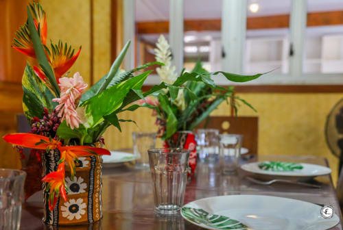 Composition florale tropicale aux fleurs rouges et roses dans un vase décoratif sur la table à manger de la villa Aimehome Moorea