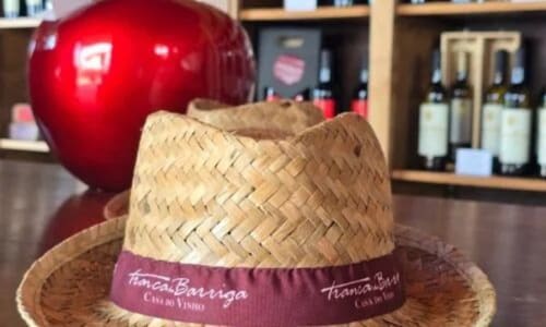 Chapéu de palha com fita vinho na Tranca da Barriga Casa do Vinho, Covilhã, com maçã decorativa vermelha e garrafas de vinho