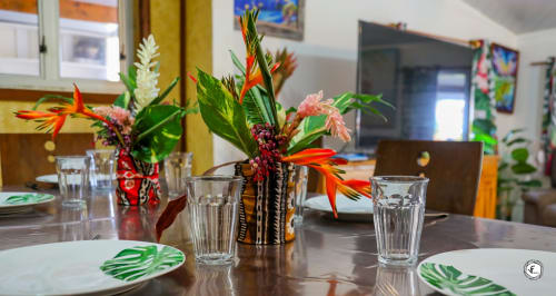 Salle à manger tropicale à la villa Aimehome Moorea avec fleurs éclatantes, couverts et verres d'eau sur table