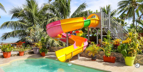 Toboggan coloré à côté d'une piscine turquoise entourée de palmiers à la villa Aimehome à Moorea